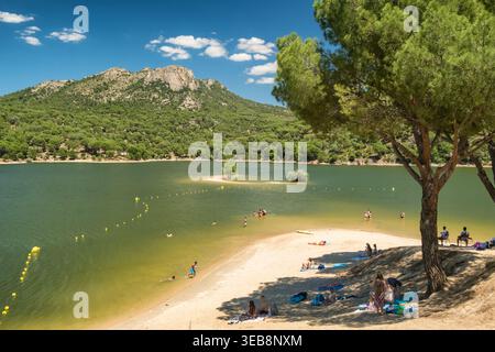 Menschen, die sich am Sandstrand am See mit Berg- und Waldhintergrund entspannen Stockfoto