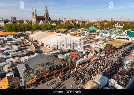 60. Münchner Frühlingsfest, Überblick vom Riesenrad bis zum Horizont, schönstes Frühlingswetter am Wochenende, München, April 2026 Deutschland, München, 17. 2026. April 60. Münchner Frühlingsfest, Blick vom Riesenrad bis zum Horizont mit Kirche St. Paul und Frauenkirche, schönstes Frühlingswetter am Wochenende, Freitag um 18 Uhr, das Abendlicht wirft lange Schatten, Sonne und Temperaturen bis 20 Grad, blauer Himmel, das traditionelle Volksfest findet zum Jubiläum diesmal erstmals für drei Wochen statt, vom 17.04. bis zum 10.05.2026, das erste Frühlingsfest Krieg 1965, Theresienwiese, blauer Bucht Stockfoto