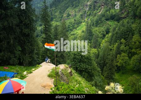 Aus einer größeren Perspektive sieht man eine Person, die friedlich auf einem hohen Punkt mit der indischen Flagge sitzt und die weite aussicht auf die sanften grünen Hügel genießt Stockfoto