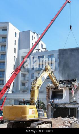 Ein gelber Bagger und ein roter Mobilkran führen Abbrucharbeiten an einem Gebäude neben Wohnwohnungen durch Stockfoto