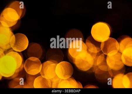 Goldene Bokeh-Lichtkreise leuchten auf einem tiefschwarzen Hintergrund und schaffen ein warmes, abstraktes Ambiente mit weichem Fokus und viel Kopierraum. Stockfoto