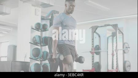 Er hält Hexen-Kurzhanteln, ein Mann mit grauem T-Shirt und Shorts, der einen gewichteten Ausfallschritt im Fitnessstudio macht, medizinische Bälle Stockfoto