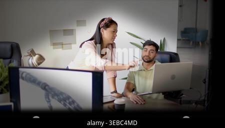 Frau, die auf Laptop und Monitor zeigt, Mann im Büro, rosa Bluse Stockfoto
