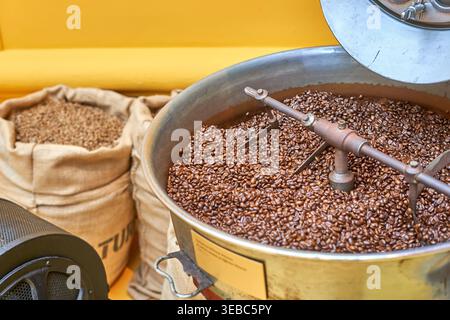 Eine Nahaufnahme von gerösteten Kaffeebohnen in einer professionellen Kaffeeröstmaschine mit sichtbaren Metallrührarmen in einer kreisförmigen Kühlwanne. Die Stockfoto