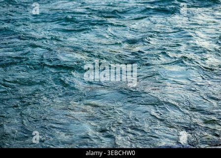 Nahaufnahme von türkisfarbenen Wasserwellen mit Sonnenlichtreflexionen. Abstrakter natürlicher Hintergrund der Fluss- oder Seenoberfläche. Stockfoto