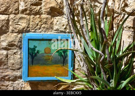 Dekorative bemalte Tafel, eingebettet in eine rustikale Steinwand mit Aloe-Pflanze, mediterrane künstlerische Details Stockfoto