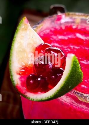 Ein knalliges pinkfarbenes Getränk in einem Glas. Der grüne Kalkkkeil liegt auf dem Rand auf. Rote gummiartige Bonbons schweben innen. Die Textur wirkt frostig und cremig. Lebendige Farben schaffen Stockfoto