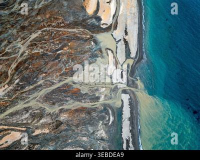 Aus der Vogelperspektive der Gletscherschmelzflüsse, die durch dunkle vulkanische Böden in den türkisfarbenen arktischen Ozean Svalbard, Svalbard und Jan Mayen fließen. Stockfoto