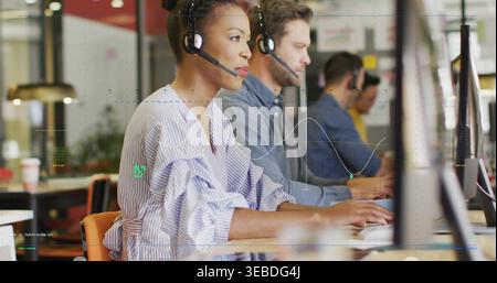 Eine Frau, die ein Headset trägt, in einer blau gestreiften Bluse, die am offenen Schreibtisch mit Monitoren arbeitet Stockfoto