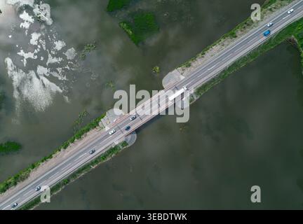 Eine Luftaufnahme zeigt eine Betonbrücke mit zwei Bahnen, die einen Fluss überquert. Mehrere Autos und ein großer LKW fahren auf der Brücke Stockfoto