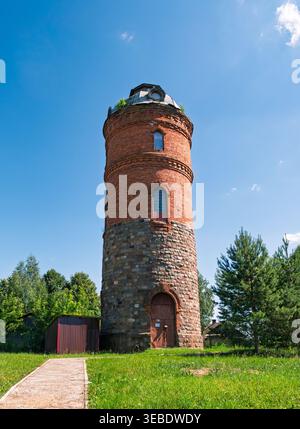 Der historische Backstein- und Steinwasserturm erhebt sich über grünem Gras unter einem hellblauen Himmel Stockfoto