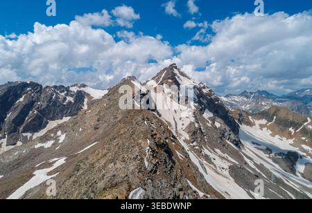 Schneebedeckte Berggipfel erheben sich vor einem blauen Himmel voller Wolken in einer abgelegenen alpinen Region Stockfoto