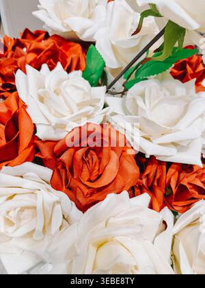 Detaillierte Nahaufnahme von roten und weißen künstlichen Rosen mit weichen Stoffblättern und grünen Blättern. Perfekt für florale Hintergründe, romantische Themen, Hochzeiten Stockfoto