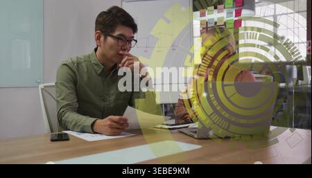 Ich überprüfe Dokumente, asiatischer Mann in grünem Hemd und Kopftuch, die Frau, die auf Laptop am Meeting-Tisch schreibt Stockfoto