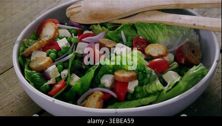 Mit weißer Keramikschale, in der Romaine-Salat auf rustikalem Holztisch gehalten wird, mit hölzernen Kellern Stockfoto