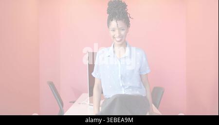 Sitzende Frau, die sich auf einem weißen Schreibtisch in einem kleinen Büro lehnt, mit hellblauem Hemd, Monitor und Stühlen Stockfoto