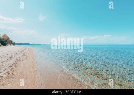 Eine ruhige Meereslandschaft mit einer klaren, ruhigen Küste mit transparentem blauem Wasser und glatten Kieselsteinen, die unter der Oberfläche sichtbar sind. Der Himmel ist hell und cl Stockfoto