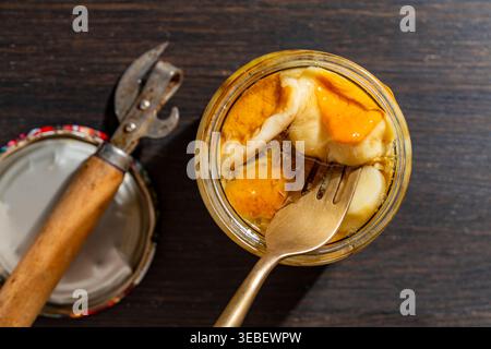 Marinierte Pilze in Glasgefäß mit Vintage-Öffner. Eingelegte Wildpilze in einem Glas mit goldener Gabel auf dunklem Holztisch. Traditionelle hausgemachte Pres Stockfoto