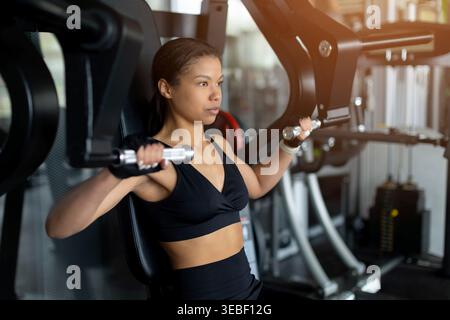 Fokussierte junge Schwarze Frau mit Brustpresse im Fitnessstudio Stockfoto