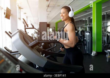 Glückliche junge Schwarze, die im Fitnessstudio auf dem Laufband läuft und lächelt Stockfoto