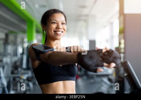 Glückliche junge Schwarze Frau im Fitnessstudio lächelt, während sie die Arme nach vorne streckt Stockfoto
