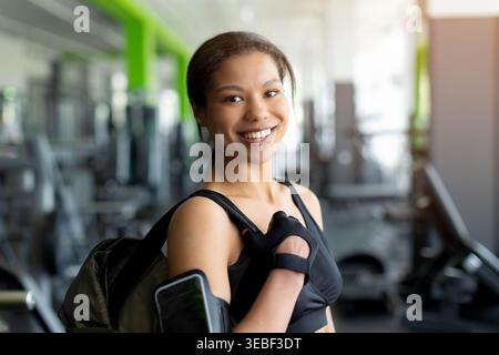 Lächelnde junge Schwarze Frau im Fitnessstudio, die Sporttasche über die Schulter trägt Stockfoto