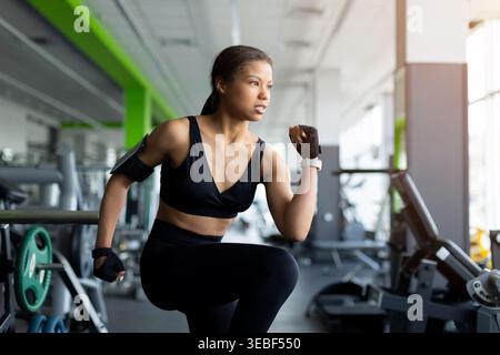 Fokussierte schwarze Frau, die im Fitnessstudio Squat-Übungen macht, mit schwarzem Sport-BH Stockfoto