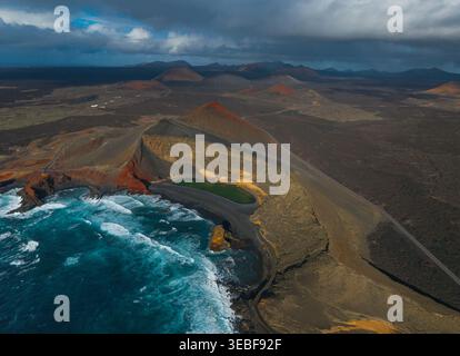Aus der Vogelperspektive die grüne Lagune des Charco de los Clicos, den schwarzen Sandstrand und die vulkanischen Krater unter einem dramatischen Himmel in Lanzarote, Kanarien, Spanien. Stockfoto