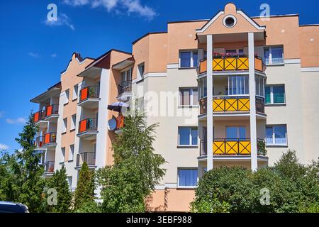 Modernes mehrstöckiges Wohnapartmenthaus mit pfirsich- und cremefarbener Fassade mit mehreren Balkonen mit orangefarbenen und gelben Dekorationen Stockfoto
