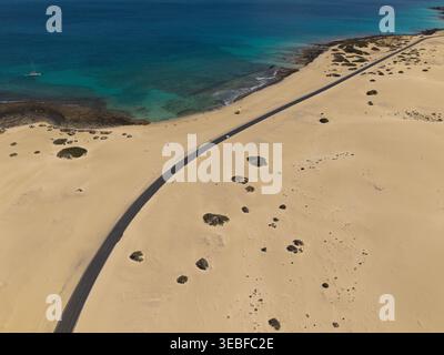 Aus der Vogelperspektive einer Straße, die sich durch weite Sanddünen entlang der türkisfarbenen Küste in Lanzarote, Kanarien, Spanien schlängelt. Stockfoto