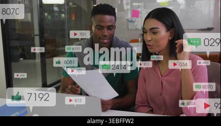 Kollegen, die Papier und Laptop im Büro untersuchen, soziale Überzüge, grüne Hemd, rosa Bluse Stockfoto