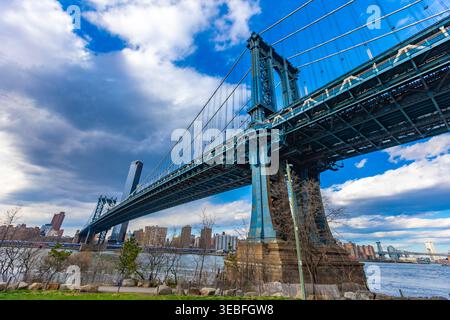 Die majestätische Manhattan Bridge überspannt den East River, eingerahmt von lebhaften Gebäuden und dynamischen Wolken, die die Schönheit von New York City zeigen. Stockfoto
