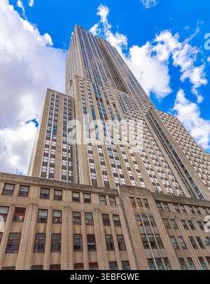 Von einem niedrigen Aussichtspunkt thront das Empire State Building majestätisch vor einem strahlend blauen Himmel voller flauschiger Wolken. Stockfoto