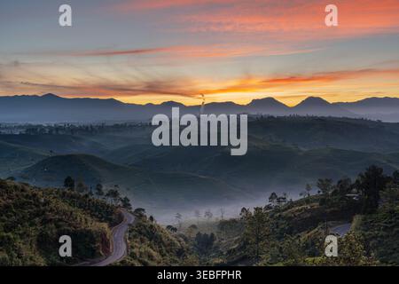 Pulsierender Blick auf den Sonnenuntergang über sanfte Teeplantagen mit einer gewundenen Straße in Cukul, Pangalengan, West Java, Indonesien Stockfoto