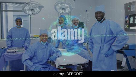Posierendes Operationsteam mit blauen Kleidern und Kappen um den OP-Tisch im Krankenhaus, mit Monitoren Stockfoto
