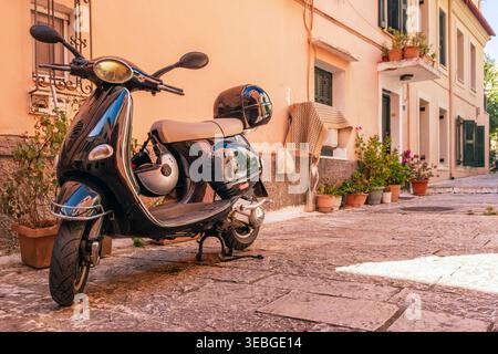 Ein Roller steht auf einer gepflasterten Gasse mit Terrakotta-Töpfen und pastellfarbenen Gebäuden in der Altstadt der Insel Korfu, Griechenland Stockfoto