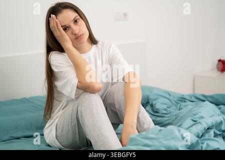 Depressive, brünette Frau, die den Kopf auf dem Bett hält und an Kopfschmerzen, Stress und Schlaflosigkeit leidet. Stockfoto