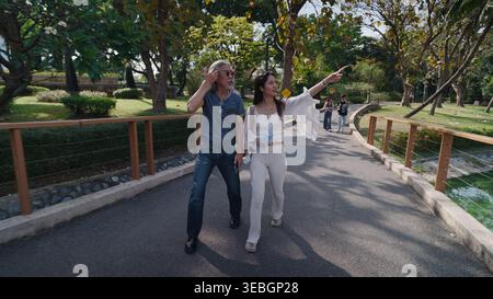 Seniorenmann und junge Frau, die in einem Park spazieren, Frau, die auf etwas Interessantes zeigt, ihren Urlaub genießt Stockfoto
