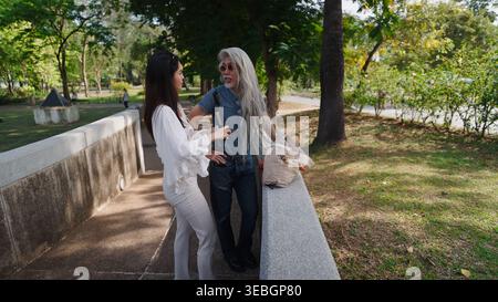Content Creator interviewt einen älteren Mann mit langen weißen Haaren in einem Park, um ansprechende Inhalte für soziale Medien zu erstellen Stockfoto