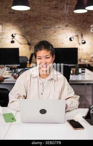 Junge asiatische Frau lächelt und arbeitet am Laptop im modernen Büro Stockfoto