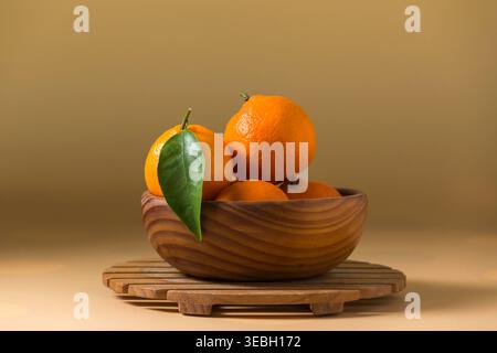 Stilleben-Komposition aus Reifen, lebendigen Mandarinen mit grünen Blättern, die in einer rustikalen Holzschale auf einem Lattenrost angeordnet sind. Sanfte Studiobeleuchtung in Crea Stockfoto