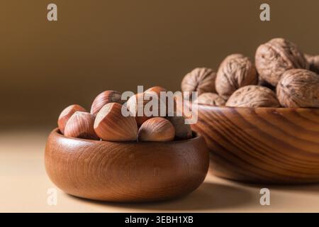 Ein sauberer, horizontaler kommerzieller Schuss roher Haselnüsse in einer kleinen Holzschale, mit einer Schüssel Walnüsse im verschwommenen Hintergrund. Sanfte Beleuchtung und Wärme Stockfoto