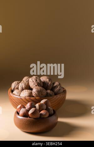 Vertikale Zusammensetzung frischer roher Haselnüsse und Walnüsse in Holzschalen auf warmem Hintergrund. Die Studio-Beleuchtung hebt satte Texturen hervor, perfekt Stockfoto