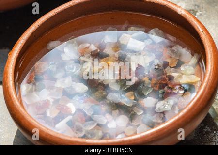 Edelsteine in Sri Lanka. Nahaufnahme von kleinen, natürlichen, hellen Steinen, die in klarem Wasser in einer rustikalen, runden Terrakotta-Schüssel getaucht sind, wodurch ein s entsteht Stockfoto