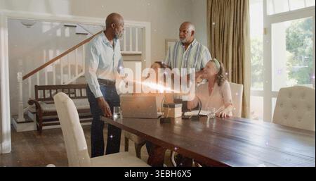 Vier Erwachsene sprechen zu Hause mit Laptop und Brille an einem Esstisch Stockfoto