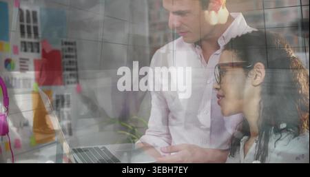 Eine Rezension in einer gemusterten Bluse mit Button-Down-Muster und Blick auf einen Laptop im Büro mit pinkfarbenen Kopfhörern Stockfoto