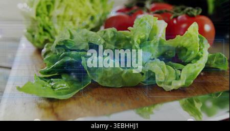 Zeigt frischen grünen Salat nass mit Tropfen auf hölzernem Schneidebrett, blauer HUD-Überzug, Tomaten Stockfoto
