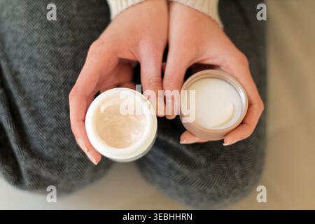Hände halten offene Gesichtscremegläser. Nahaufnahme der Hände mit zwei offenen Kosmetikgläsern, die Hautpflegetextur, Feuchtigkeitscreme und Schönheitsroutine zeigen Stockfoto