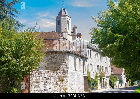 MARTEL, FRANKREICH, 3. AUGUST 2025: Blick auf eine Straße im historischen Zentrum mit befestigtem mittelalterlichen Glockenturm der Eglise Saint Maur, Departement Lot, Stockfoto