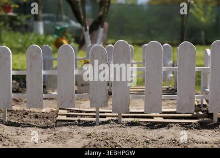 Weißer Holzpfahlzaun in einem Garten mit frisch umgewandeltem Boden, verschwommenem Grün und Bäumen im Hintergrund unter natürlichem Tageslicht 2026 Stockfoto